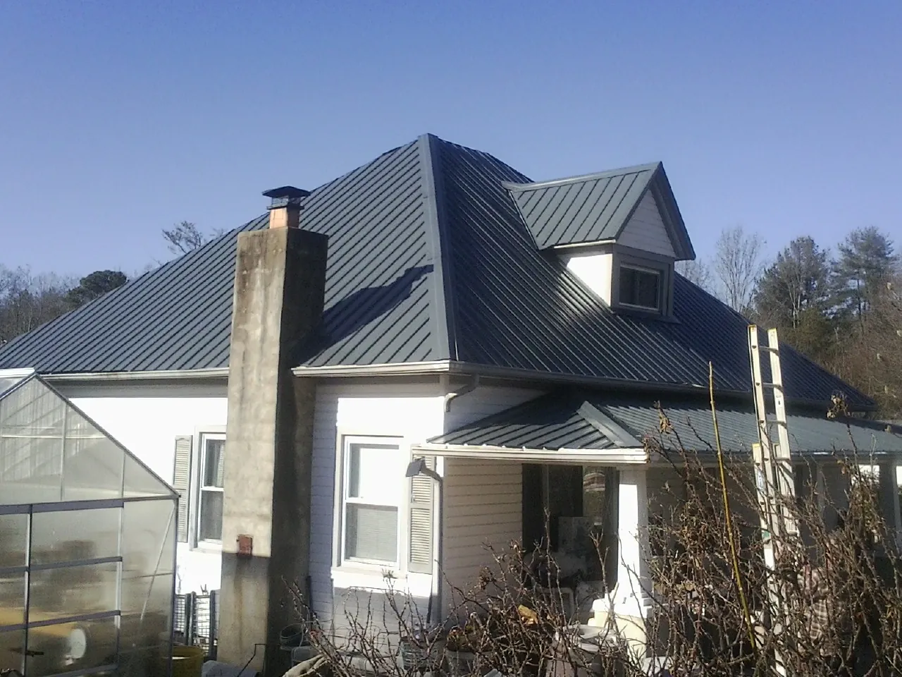 Dark blue standing seam metal roof on a white farmhouse with dormer — Slate & Tile Roof Repair by Roofing Brothers in Herreid