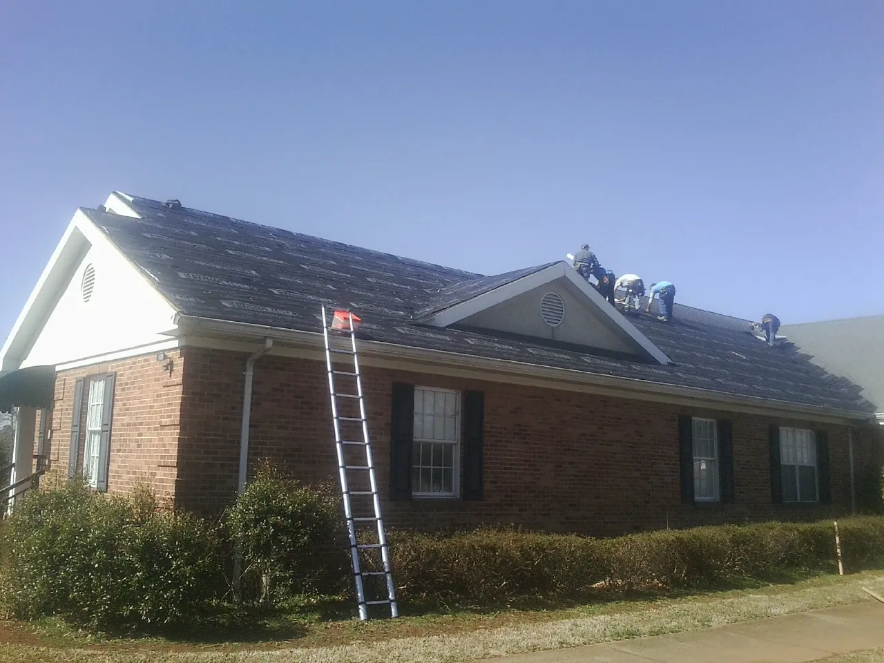 Crew tearing shingles off a brick ranch roof with a ladder set — Emergency Roof Repair work by our crew in Herreid