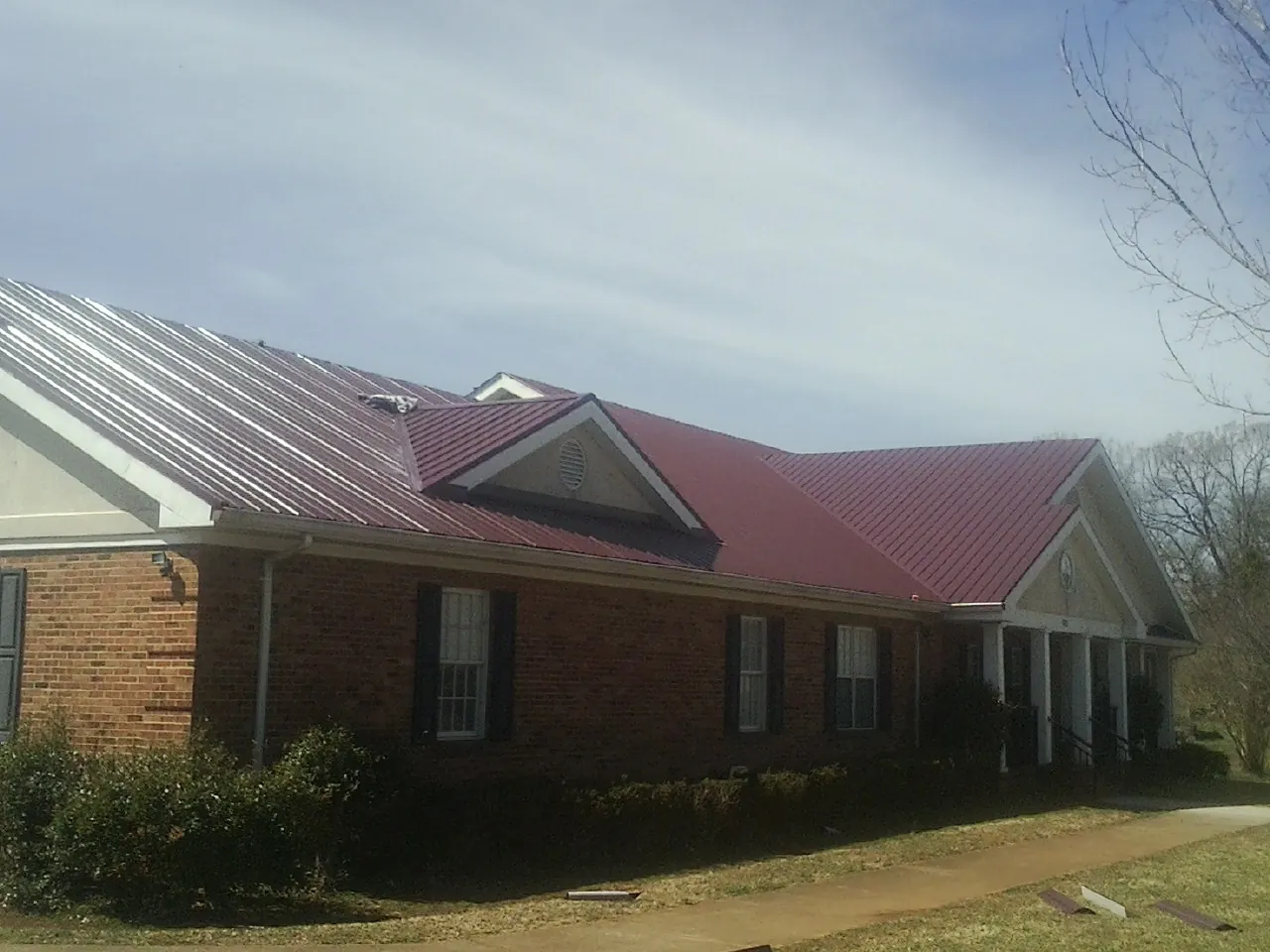 Red metal roof with gabled entries on a long brick building, from a Hail Damage Roof Repair job in Herreid