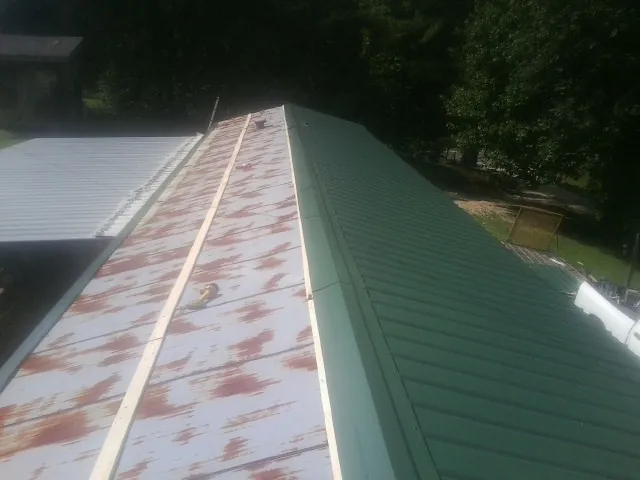 Old rusted panels beside newly installed green metal roofing — Wind Damage Roof Repair by Roofing Brothers in Herreid