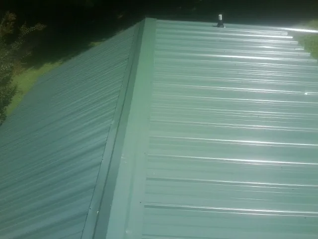 New green metal panels meeting at the ridge of a roof — Flat Roof Repair work by our crew in Herreid