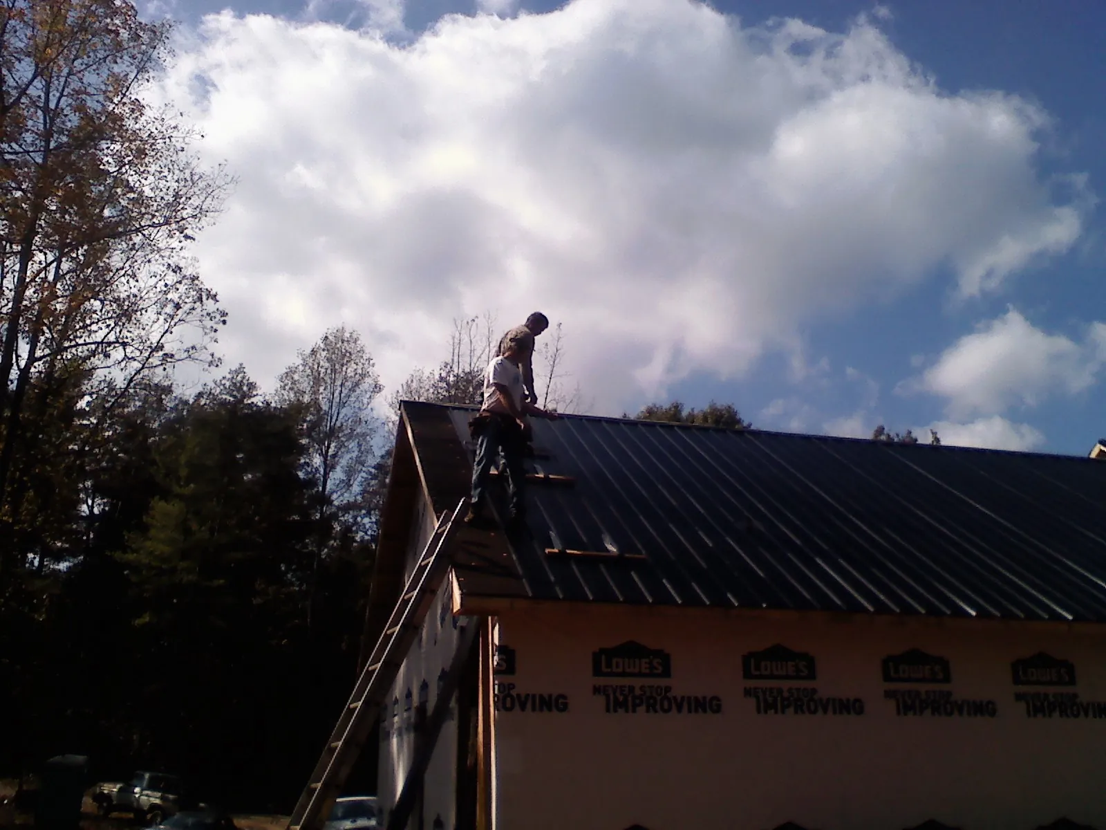 Roofer fastening dark metal panels high against a cloudy sky, from a Roof Inspection job in Herreid