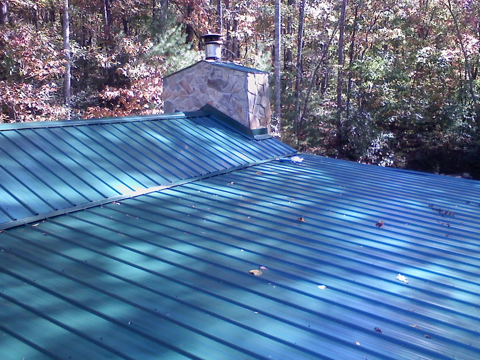 New green metal roof and stone chimney surrounded by autumn woods in Herreid