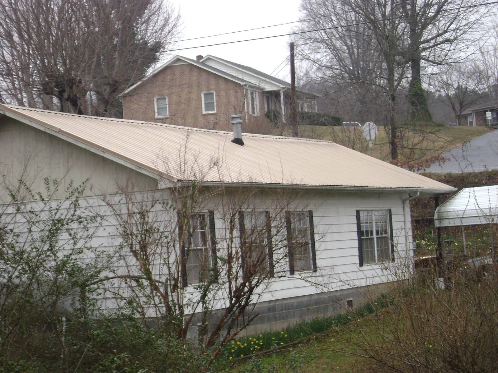 Tan metal roof on a white sided house set into a hillside — Commercial Roofing by Roofing Brothers in Herreid